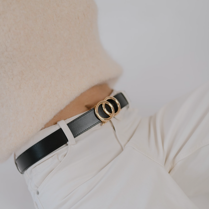 Affra Black leather adjustable women’s belt with gold double-ring buckle styled with white pants and a beige knit sweater