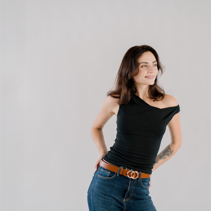 Affra tan leather adjustable women’s belt with gold double-ring buckle styled with a black sleeveless top and blue jeans on a plain background